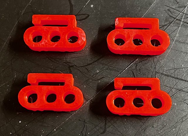 Four red plastic triple-hole cord locks